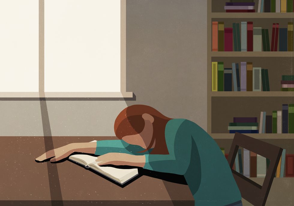 tired college student sleeping on book at sunny table in library