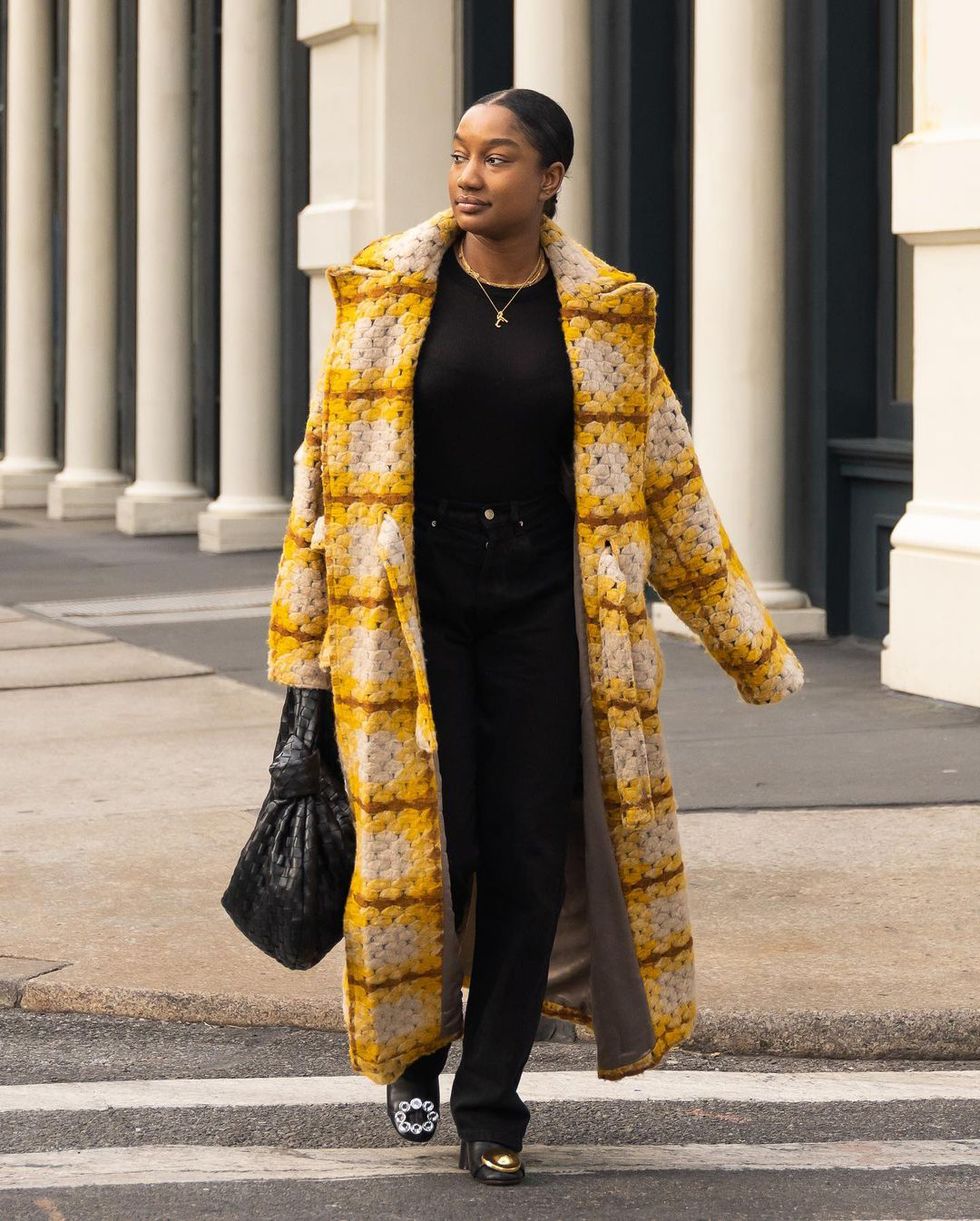 a black woman wearing a yellow coat walking down a city street